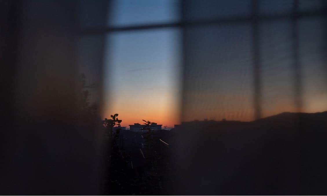 ぼやけた窓枠越しに見る、夕焼けの街のシルエット。
